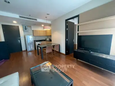 Modern open-layout living room with kitchen, wooden flooring, and sleek furniture.