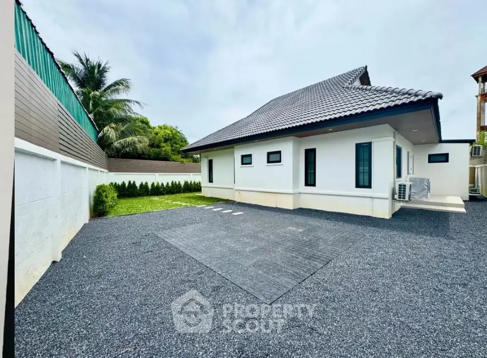 Modern single-story house with spacious gravel driveway and lush greenery.
