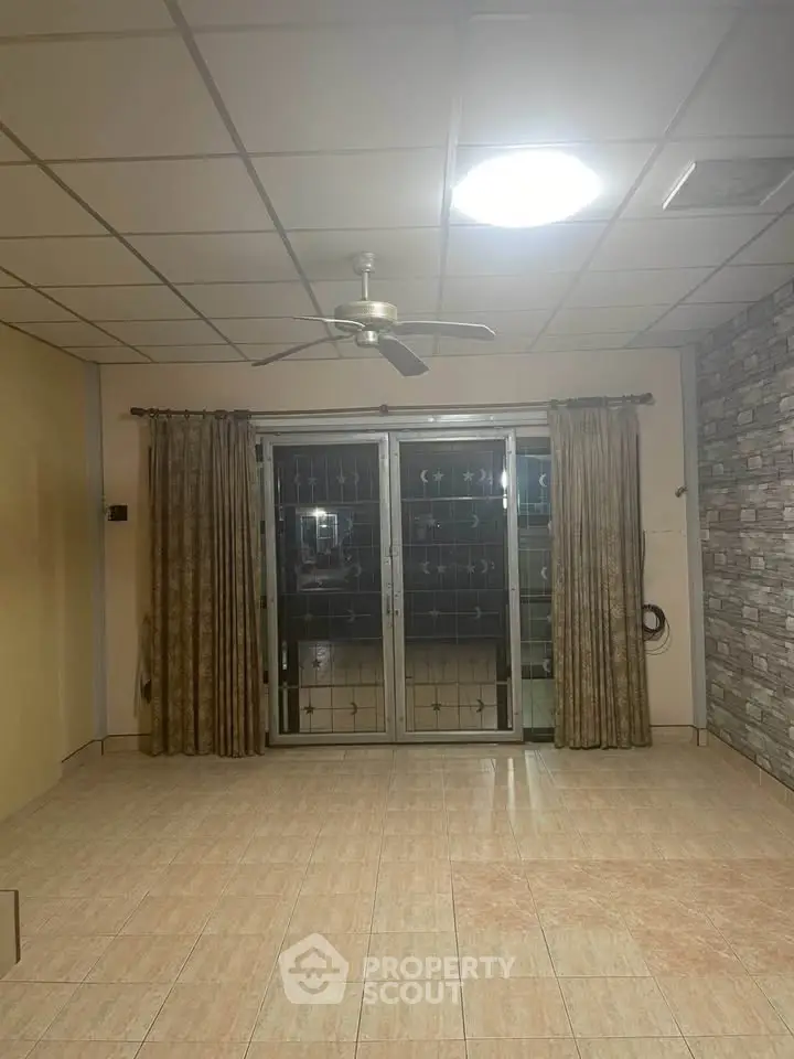Spacious living room with tiled floor, ceiling fan, and large sliding glass doors.