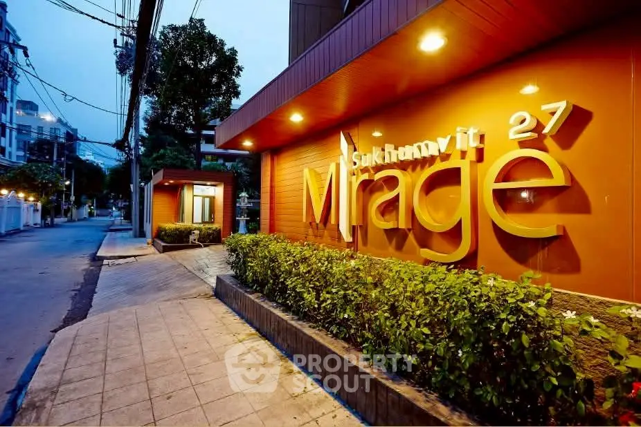 Modern building entrance with vibrant signage and lush greenery at Sukhumvit 27 Mirage.
