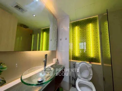 Modern bathroom with stylish glass sink and illuminated green tile accent wall.