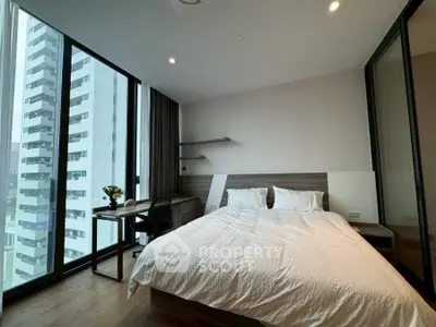 Modern bedroom with large windows and city view, featuring a cozy bed and study desk.
