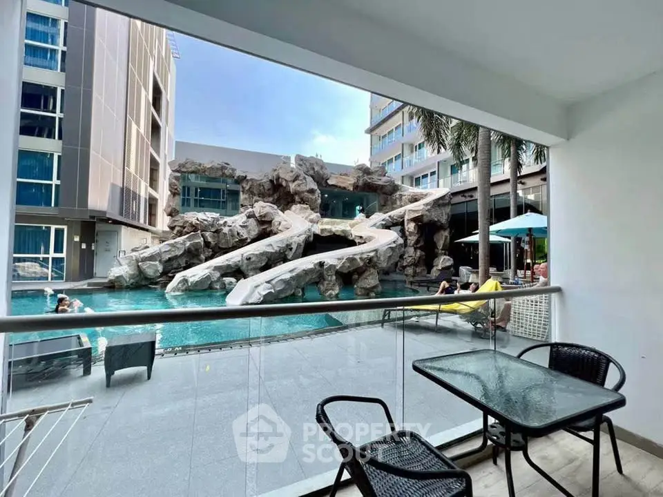 Luxurious poolside view from a modern balcony with stylish furniture and stunning rock waterfall feature.