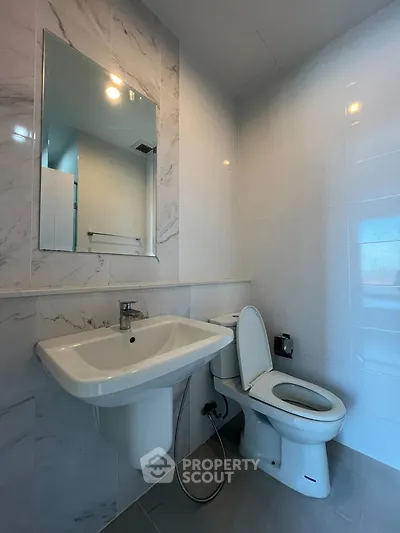 Modern bathroom with sleek fixtures and marble tiles, featuring a wall-mounted sink and toilet.