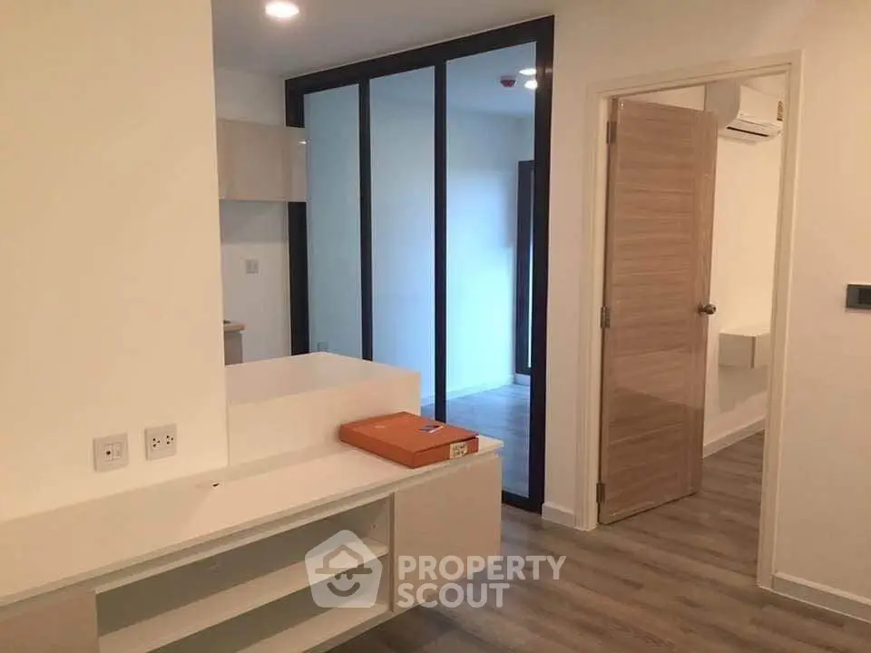 Modern apartment interior with sleek design and wooden flooring, featuring a sliding glass door and built-in storage.