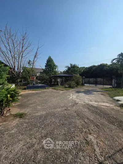 Spacious outdoor area with lush greenery and paved driveway, perfect for serene living.