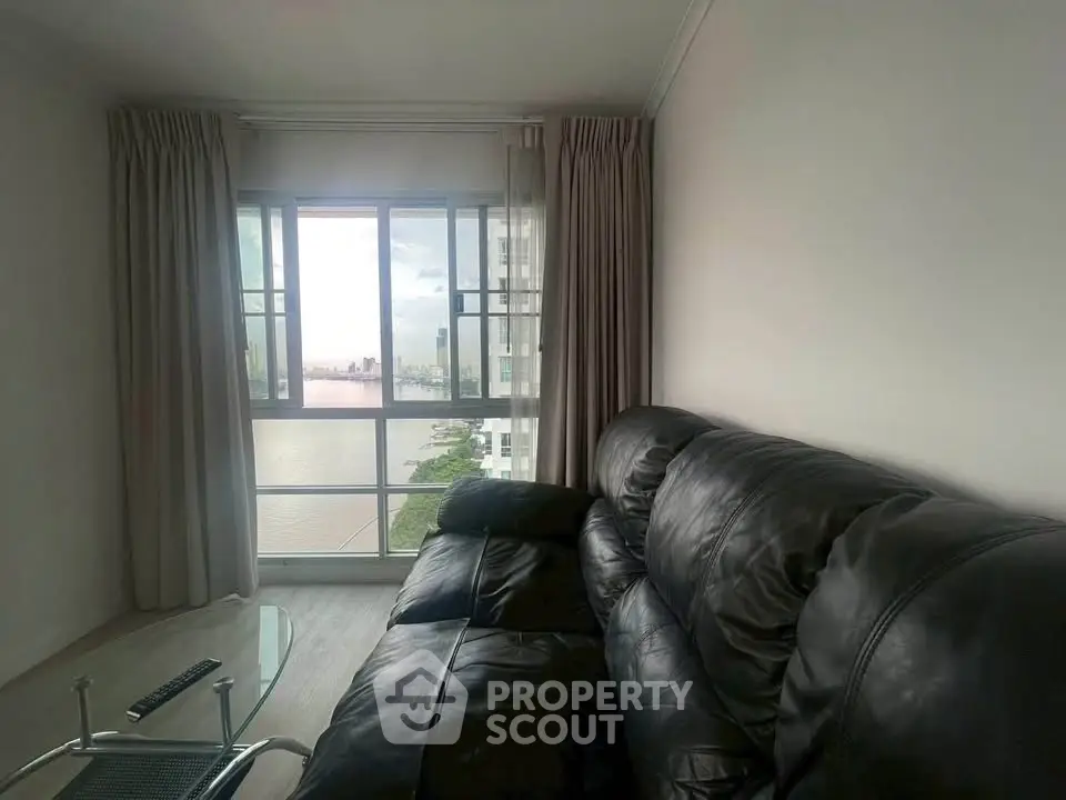 Spacious living room with leather sofa and stunning river view through large windows.