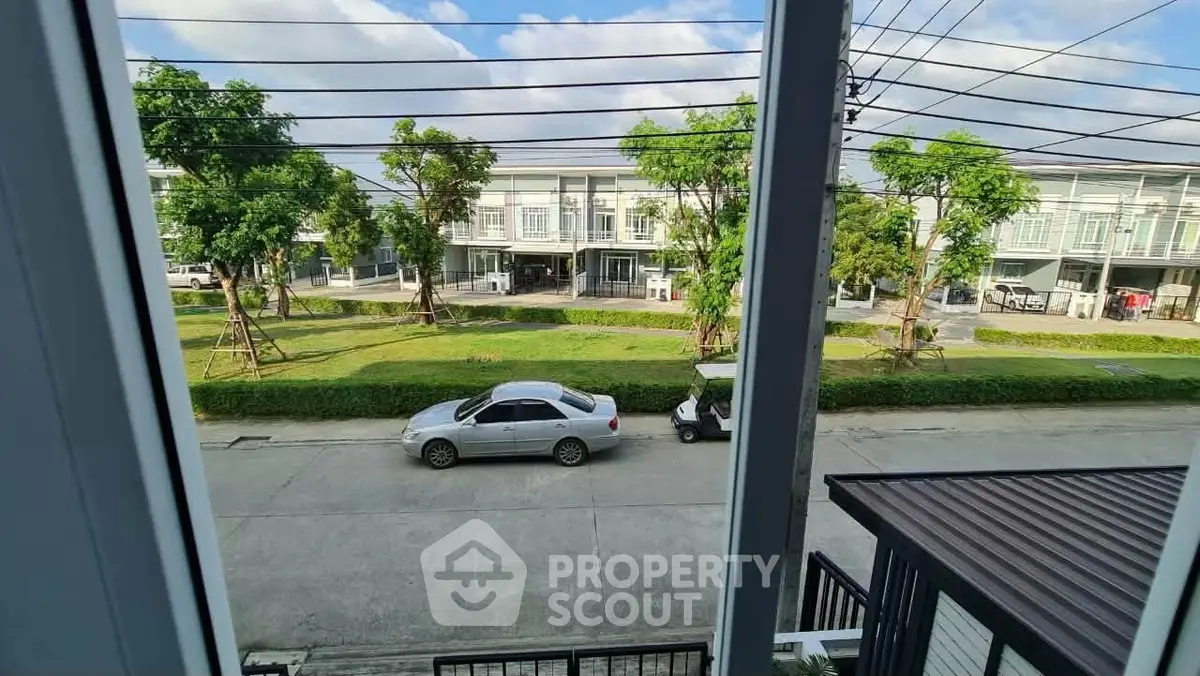 Charming view from a modern townhouse balcony overlooking a serene street and lush greenery.