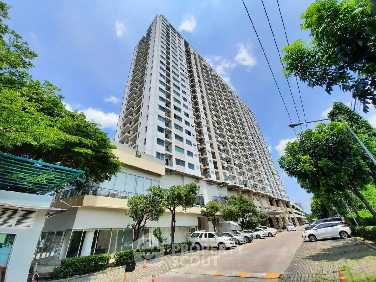 Modern high-rise residential building with lush greenery and ample parking space.