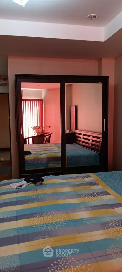 Cozy bedroom with colorful bedding and mirrored wardrobe reflecting natural light.