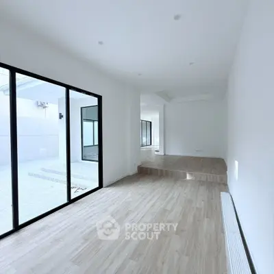 Spacious modern living room with wooden flooring and large glass doors opening to a patio.