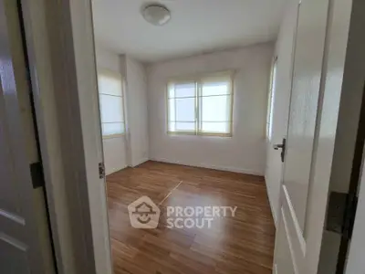 Spacious empty bedroom with wooden flooring and large windows.