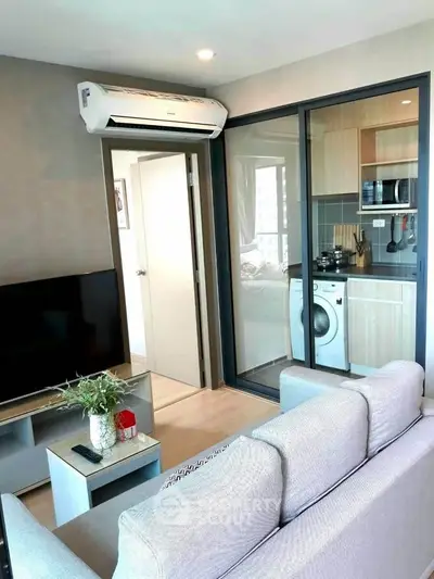 Modern living room with air conditioning and view into a compact kitchen with washing machine.