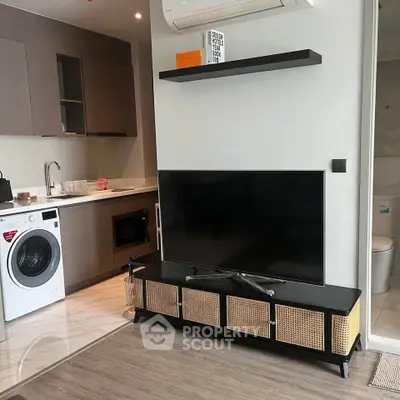 Modern apartment interior with sleek kitchen and cozy living area featuring a flat-screen TV and washing machine.