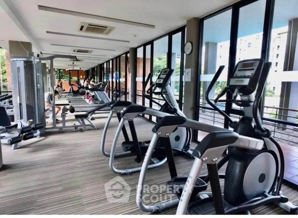 Spacious gym with modern equipment and large windows in a residential building.