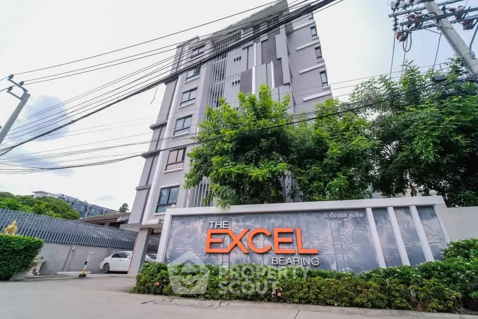 Modern condominium building exterior with lush greenery and prominent signage.