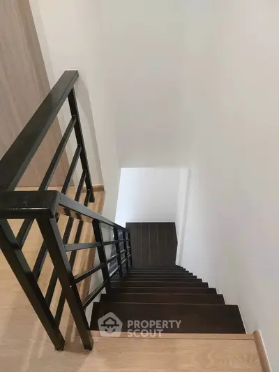 Modern staircase with sleek black railing and wooden steps in a contemporary home.