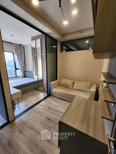 Modern apartment interior with cozy living room and bedroom separated by glass partition, featuring wooden flooring.