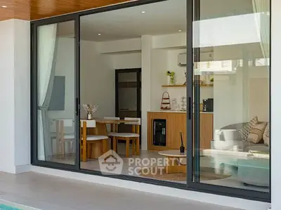 Modern living room with glass sliding doors opening to a poolside view, featuring stylish furniture and decor.