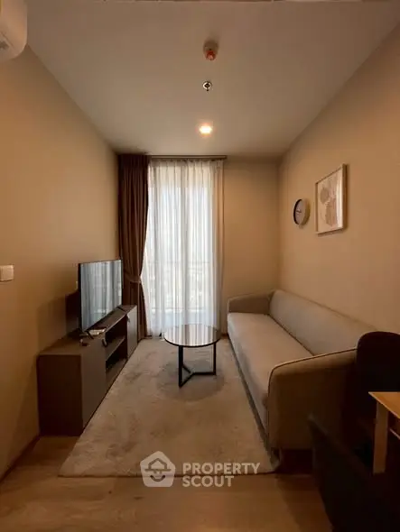 Cozy living room with modern sofa, TV, and natural light from large window.