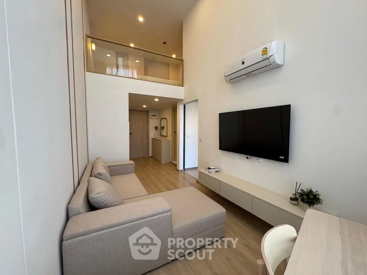 Modern living room with high ceiling and mezzanine, featuring a sleek sofa and wall-mounted TV.
