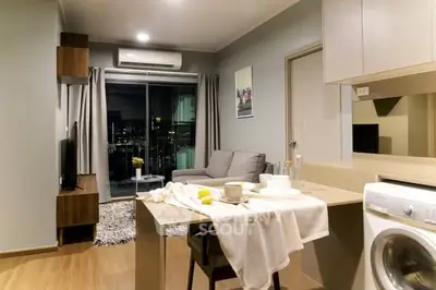 Modern living room with open kitchen and washing machine, featuring cozy seating and city view.