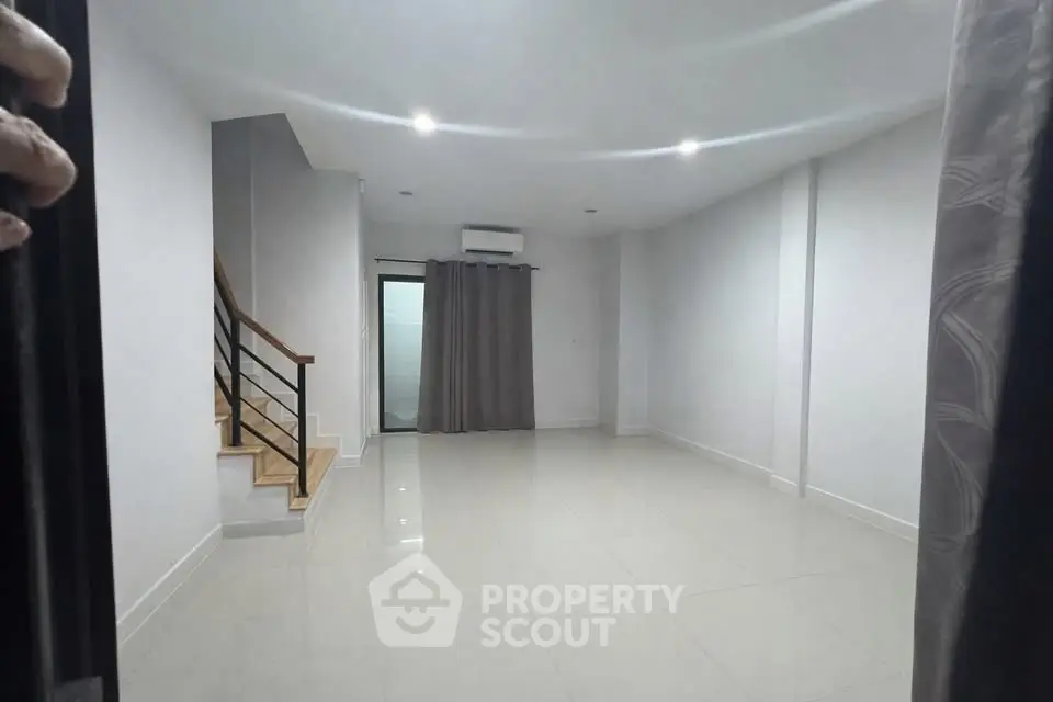 Spacious modern living room with sleek staircase and large window, perfect for contemporary living.