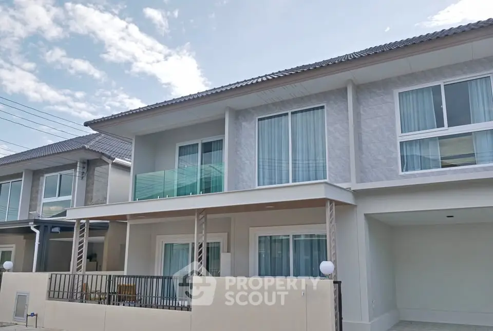 Modern two-story house with balcony and large windows under a clear blue sky.