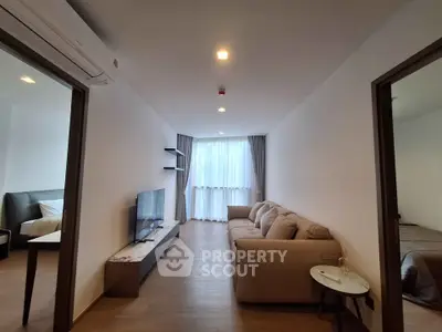 Modern living room with cozy sofa and TV, adjacent to a stylish bedroom, featuring elegant decor and natural light.