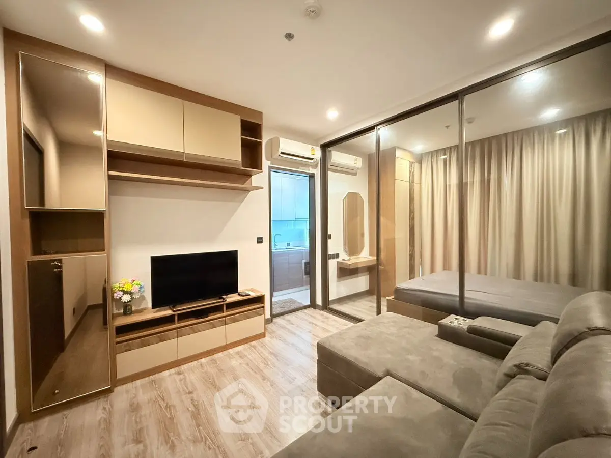 Modern living room with cozy sofa and TV, adjacent to a stylish bedroom with glass partition.
