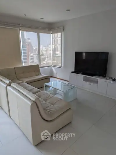 Modern living room with city view, featuring sleek white furniture and a large flat-screen TV.