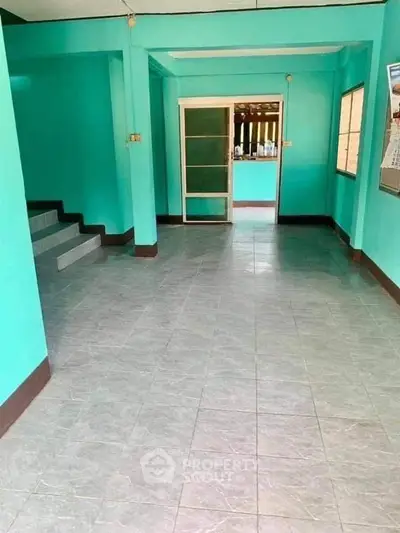 Spacious interior with vibrant turquoise walls and tiled flooring, featuring a staircase and glass door.