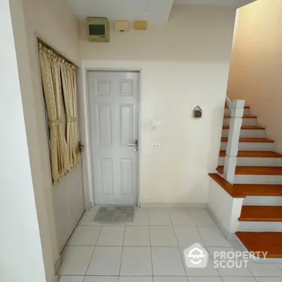 Bright and welcoming entryway with staircase leading to upper levels, featuring clean white tiles and a secure front door.