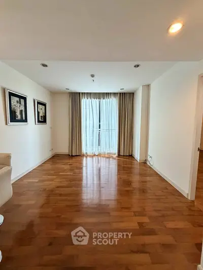 Spacious empty living room with wooden flooring and large window for natural light.