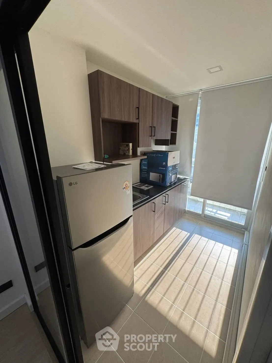 Modern kitchen with sleek cabinetry and stainless steel fridge in a sunlit apartment.