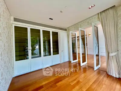 Spacious living room with elegant wooden flooring and large glass doors opening to a bright area.
