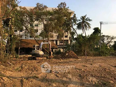 Vacant land with construction equipment and building in the background, ideal for development.