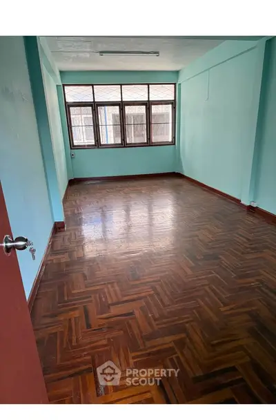 Spacious empty room with wooden parquet flooring and large windows, ideal for customization.