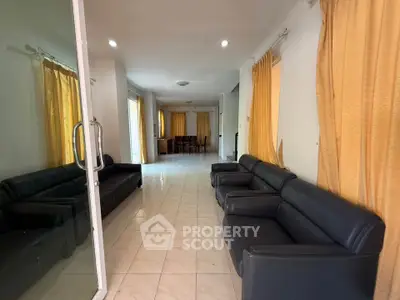 Spacious living room with black leather sofas and large windows with yellow curtains.