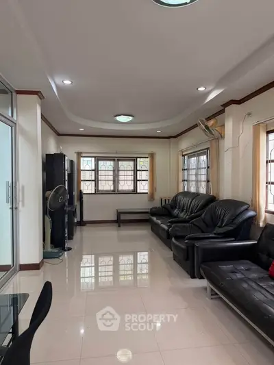 Spacious living room with modern black leather sofas and large windows for natural light.