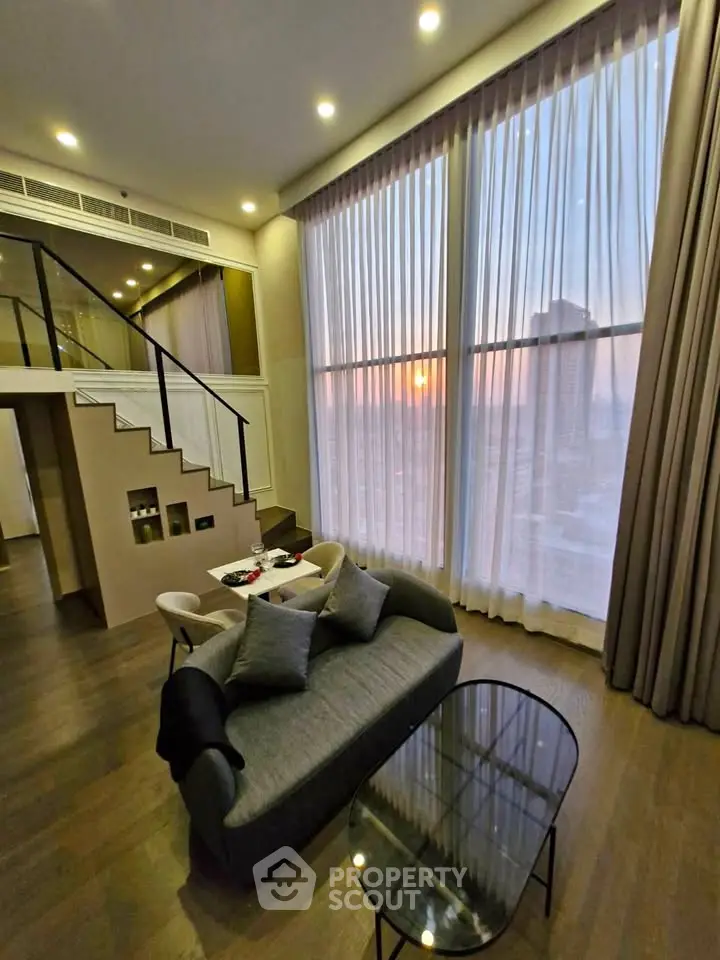 Luxurious duplex living room with high ceilings and stunning sunset view through large windows.
