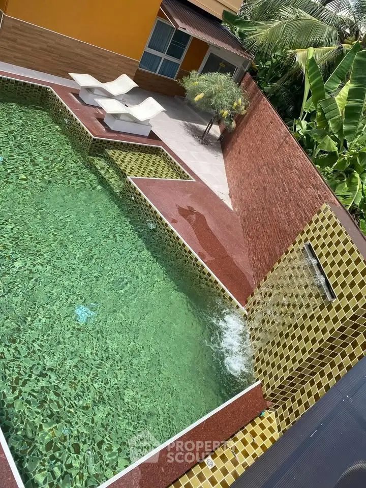 Luxurious private pool with waterfall feature and sun loungers in tropical setting.