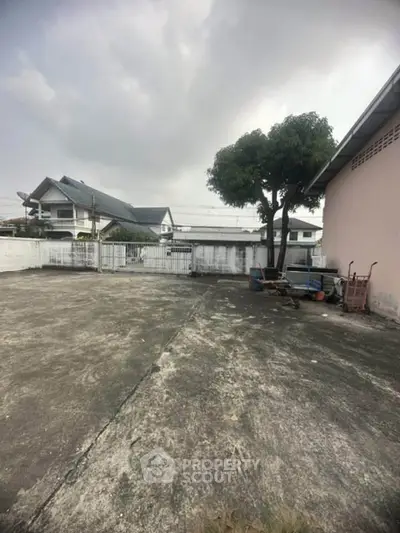 Spacious outdoor area with concrete surface and tree, ideal for parking or garden setup.