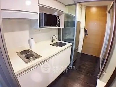 Compact modern kitchen with sleek white cabinetry and built-in appliances in a cozy apartment.