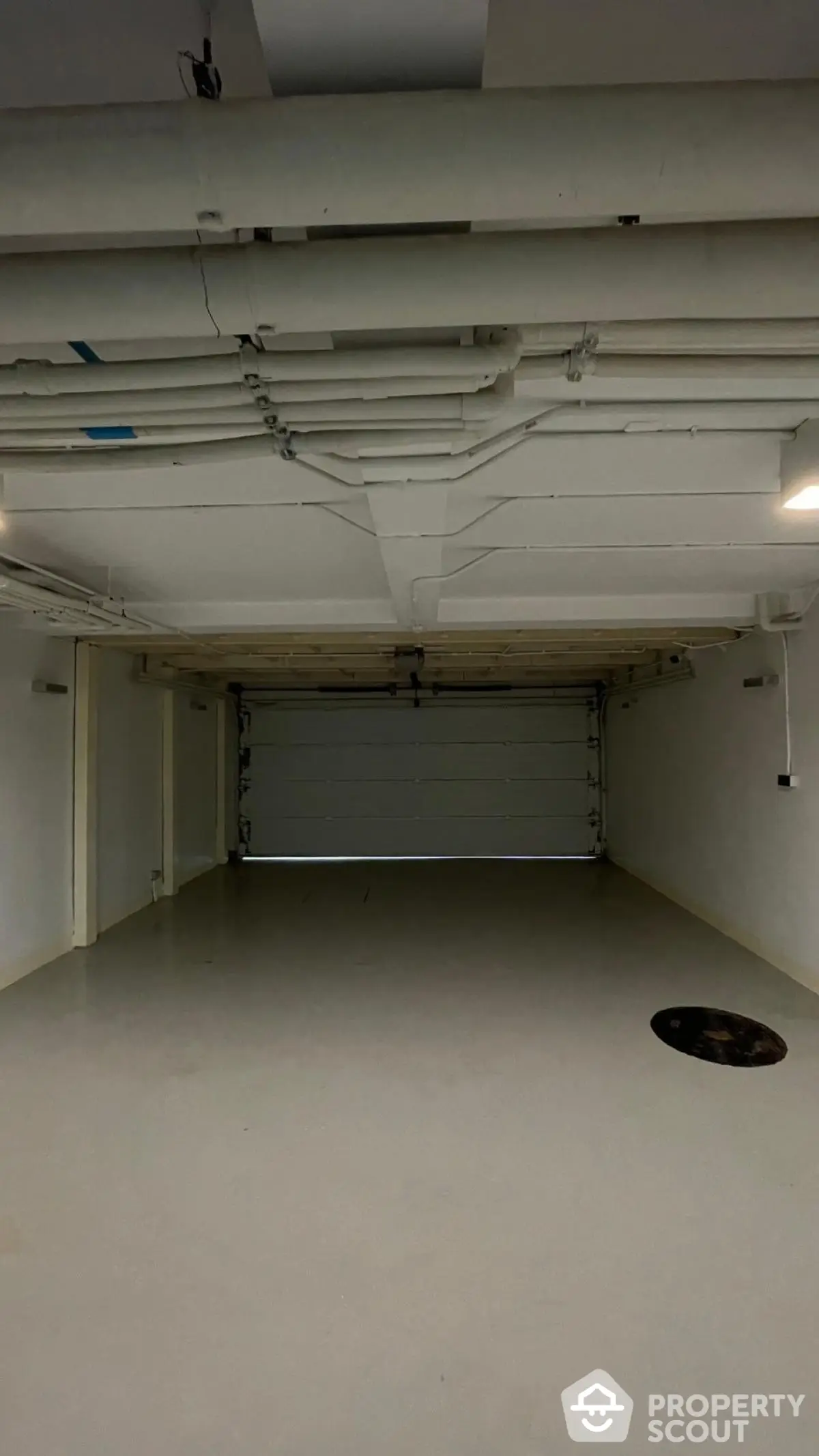 Spacious underground parking garage with clean white walls and ceiling pipes.