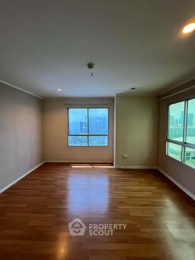 Spacious empty living room with wooden flooring and large windows offering city views.