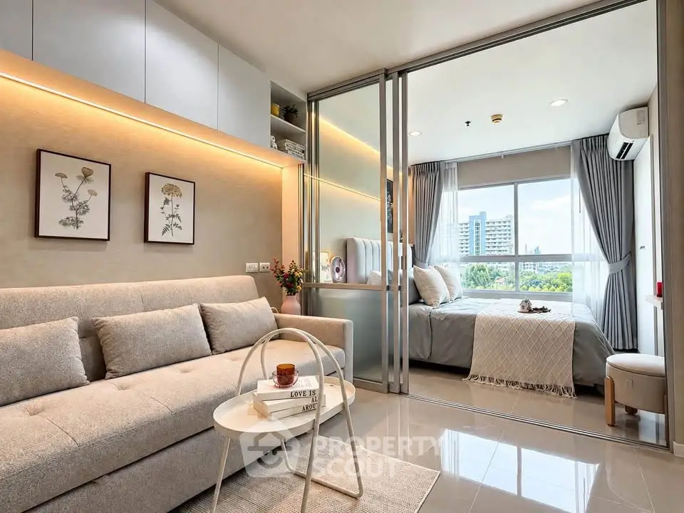 Modern open-plan living room with cozy sofa and sliding glass doors to a bright bedroom with city view.