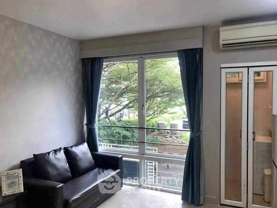 Modern living room with large window and air conditioning, offering a serene view of greenery.
