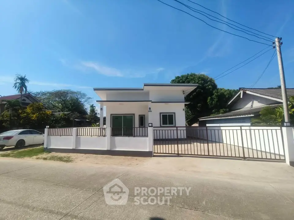 Modern single-story house with gated driveway and clear blue sky.
