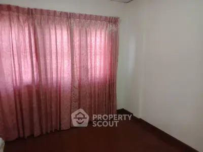 Spacious empty room with elegant pink curtains and wooden flooring.